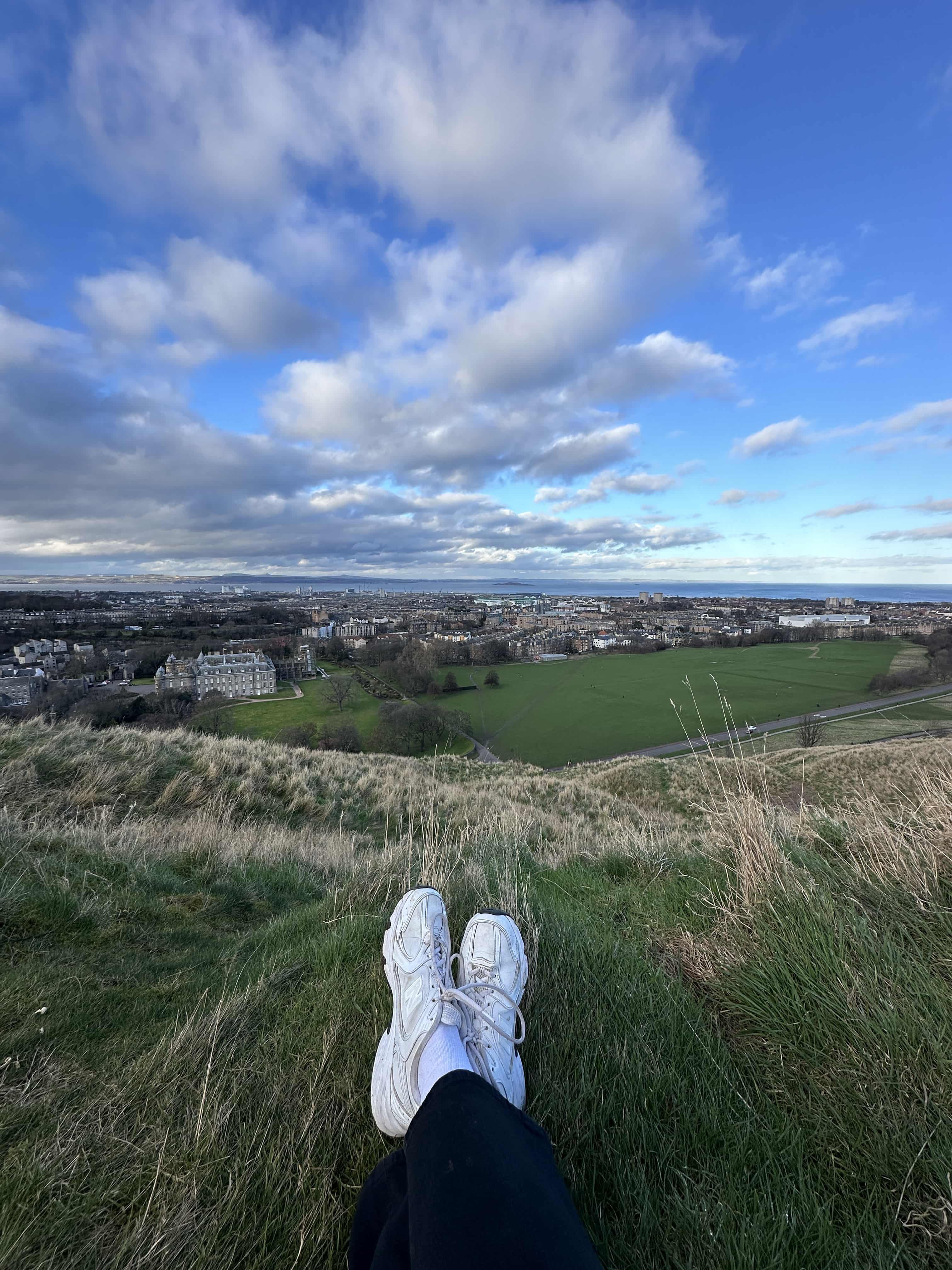 pov of a hiker with white trainers sitting on top of a hill enjoying the view of the city of Edinburgh