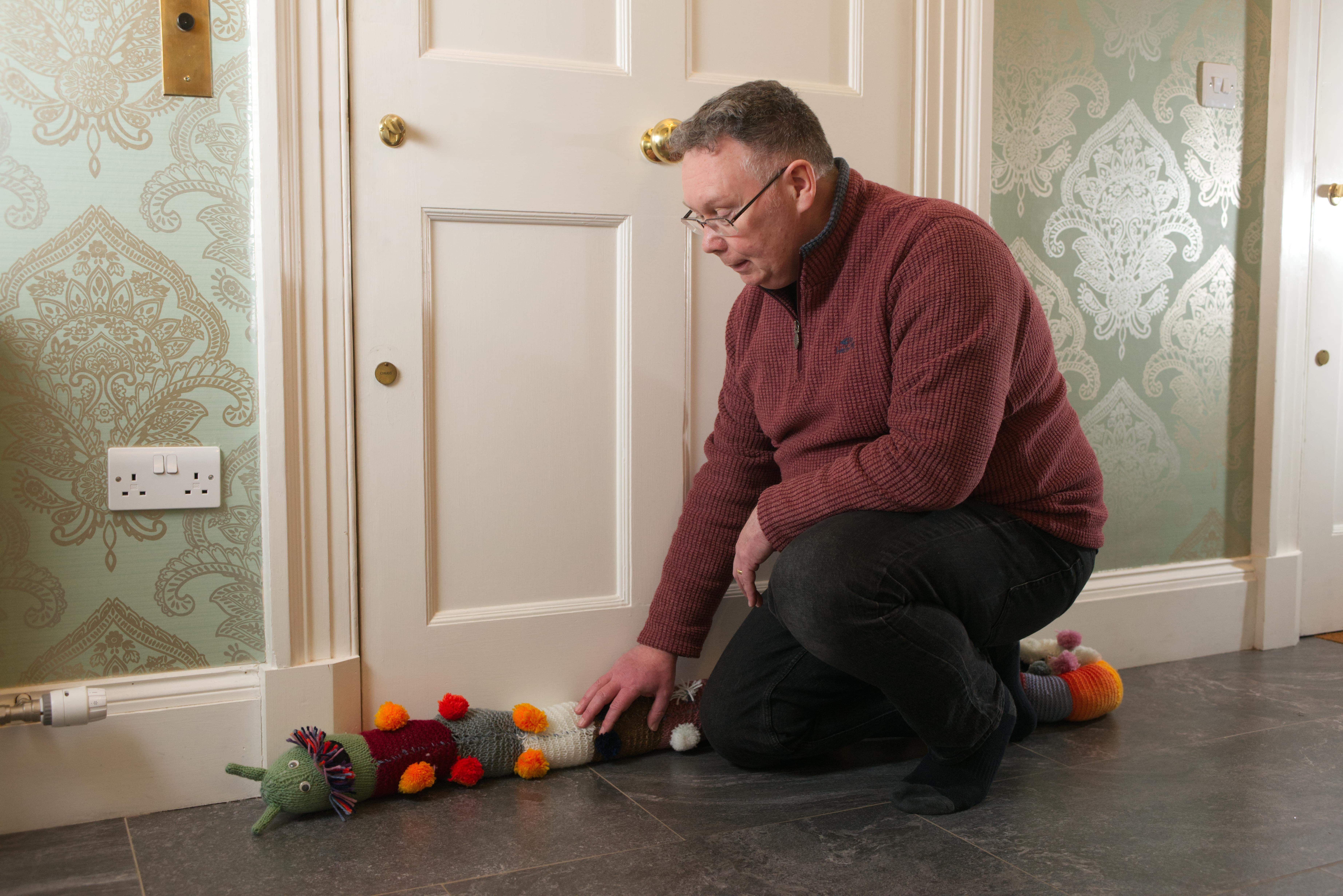 An old man laying down a caterpillar draught excluder by his door in his home