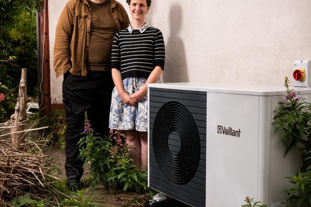 A man and a woman smiling and standing next to their heat pump outside their home