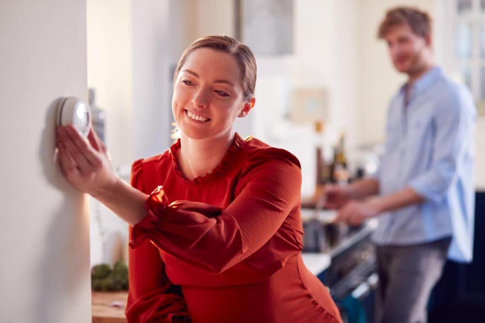 Picture of a smiling lady in red blouse turning down a thermostat