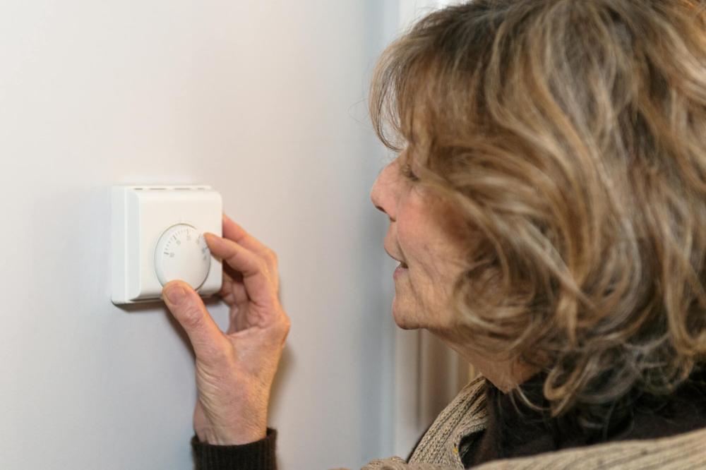 An older woman with short, light brown hair adjusts the heating controls in her house