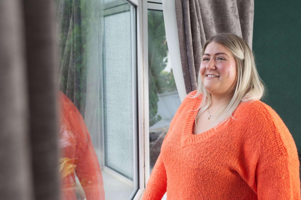 Woman wearing bright orange jumper smiles while looking out of her double glazed window